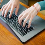 Close-up of hands typing on a laptop keyboard at a wooden table, perfect for remote work concepts.