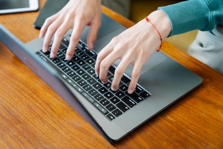Close-up of hands typing on a laptop keyboard at a wooden table, perfect for remote work concepts.